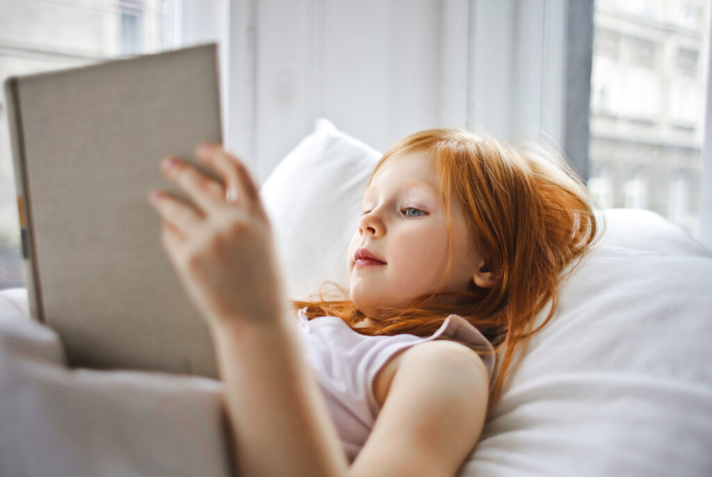 A Girl Reading A Book While Lying On Bed