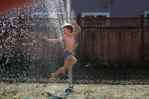 little boy jumping through sprinkler